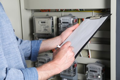 Photo of Technician worker with clipboard inspecting electricity meter, closeup