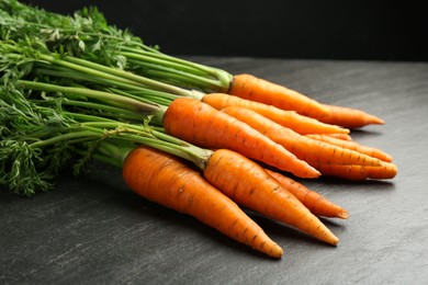 Photo of Tasty ripe juicy carrots on dark gray textured table, closeup