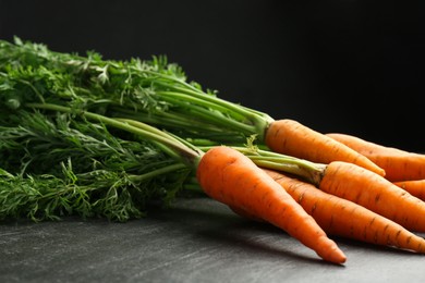 Photo of Tasty ripe juicy carrots on dark gray textured table, closeup