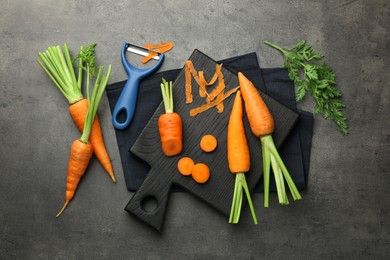 Photo of Fresh carrots, vegetable peeler and peels on gray textured table, flat lay