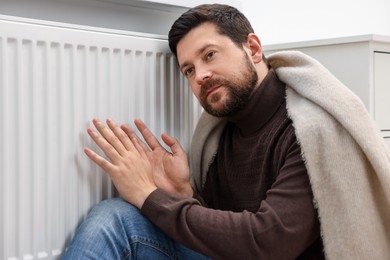 Photo of Man with blanket warming near heating radiator at home