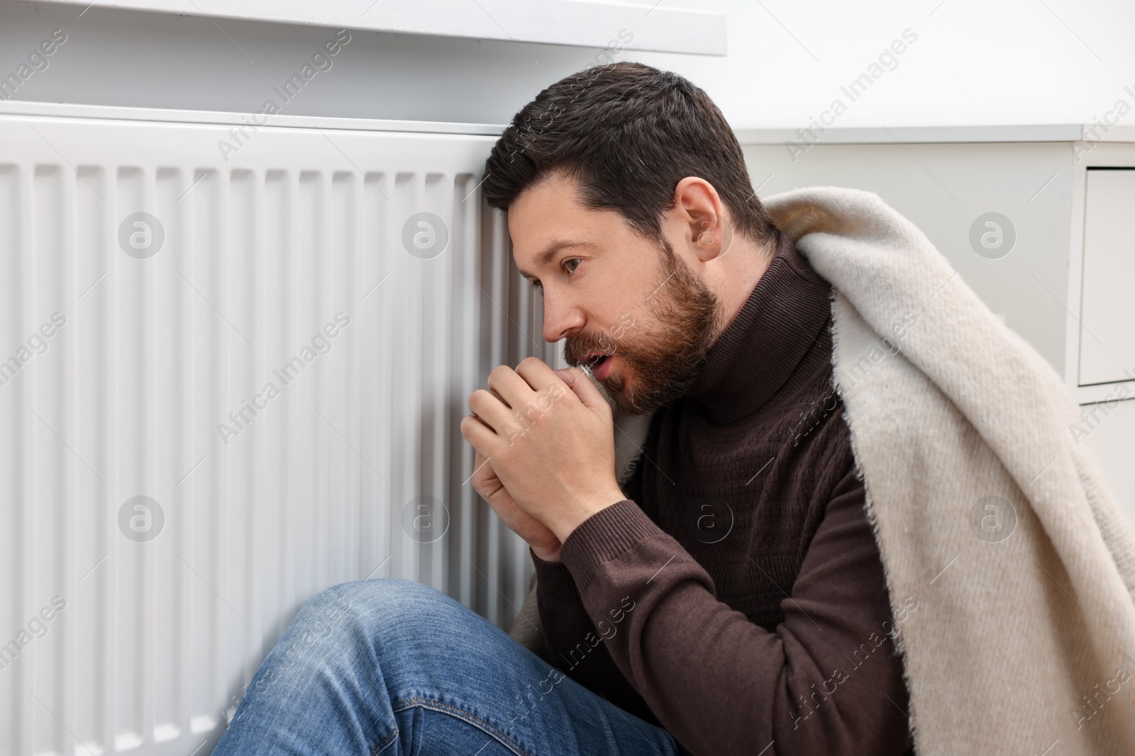 Photo of Man with blanket warming near heating radiator at home