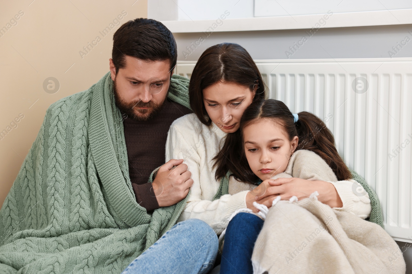 Photo of Family with blankets warming near heating radiator at home