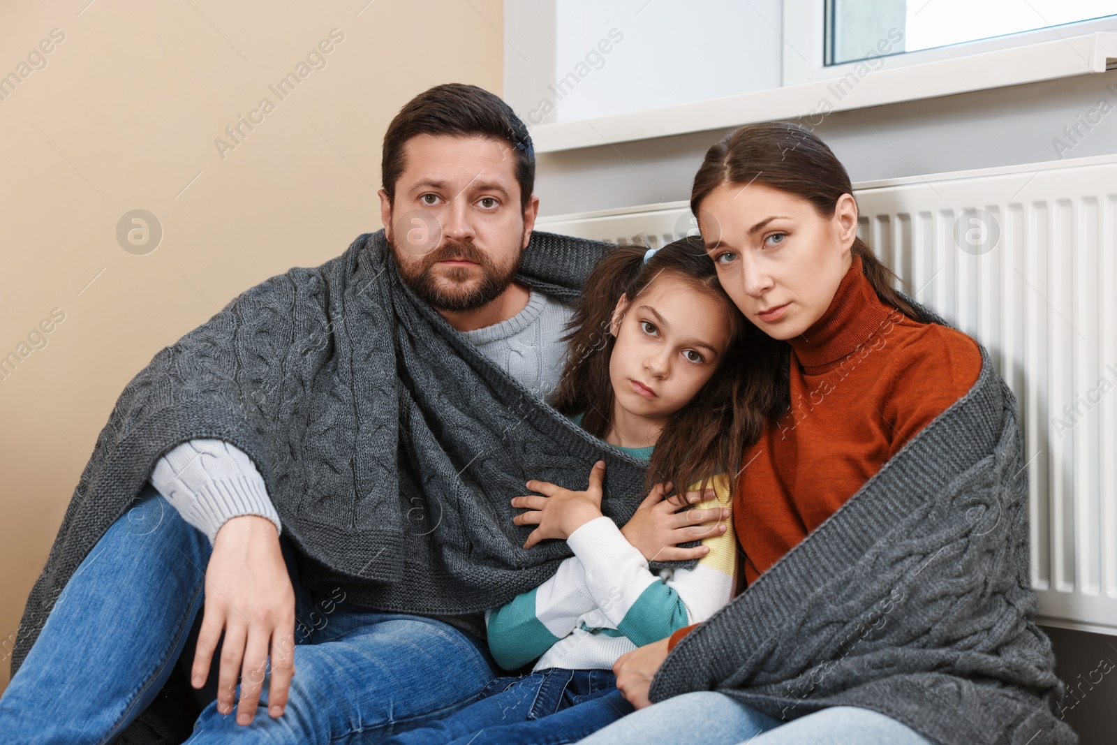 Photo of Family with blanket warming up near heating radiator at home