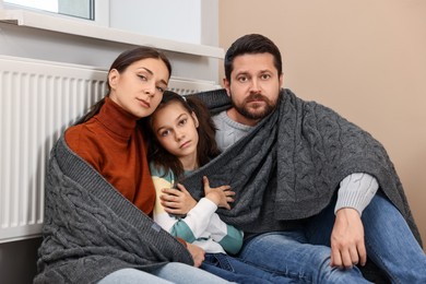 Family with blanket warming up near heating radiator at home