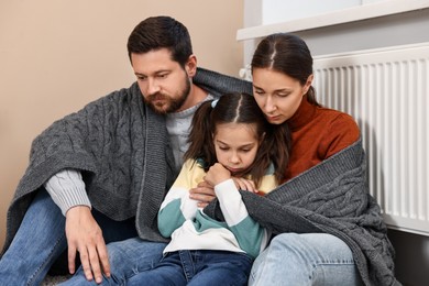 Family with blanket warming up near heating radiator at home