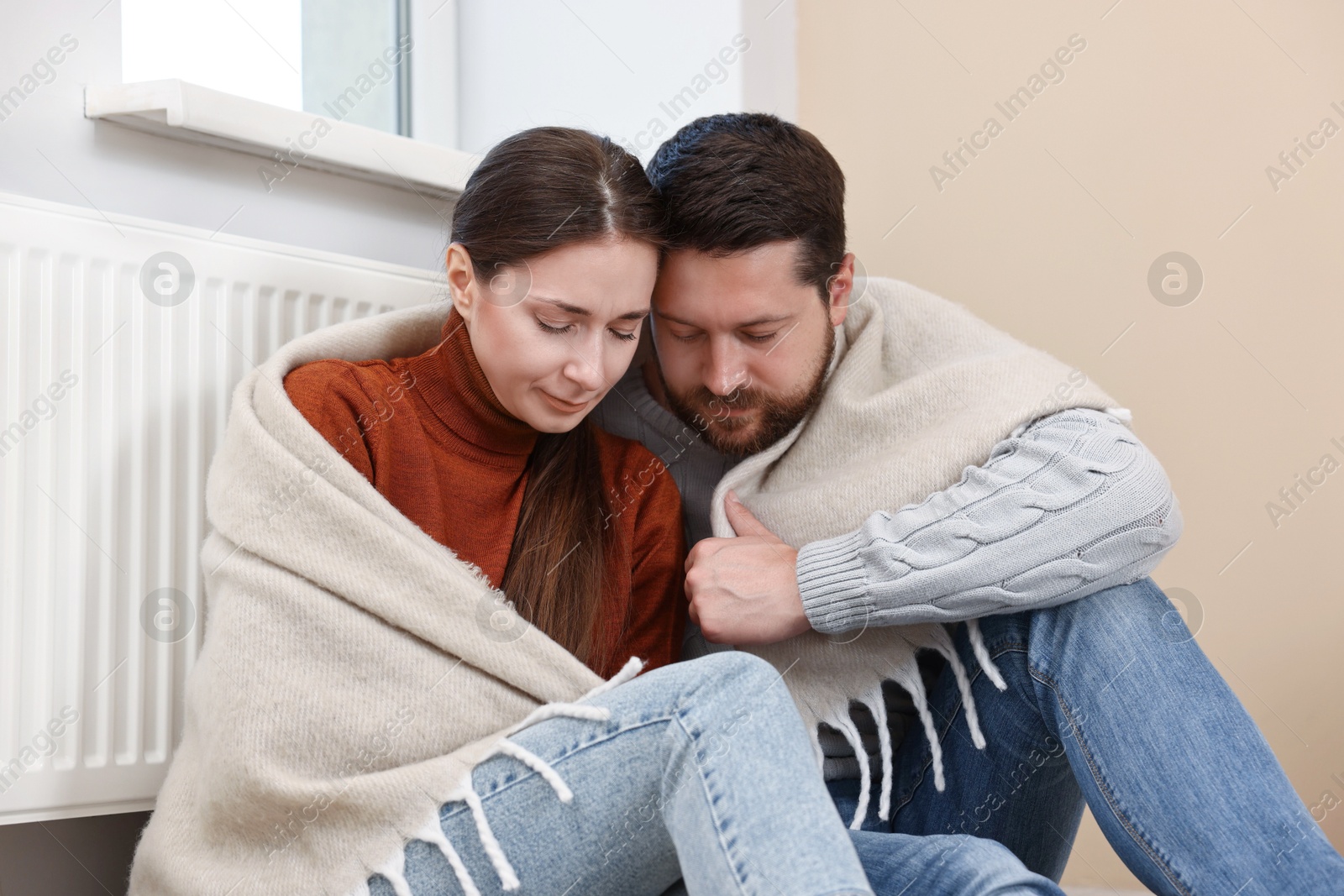 Photo of Couple with blanket warming up near heating radiator at home