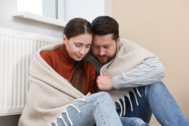 Couple with blanket warming up near heating radiator at home