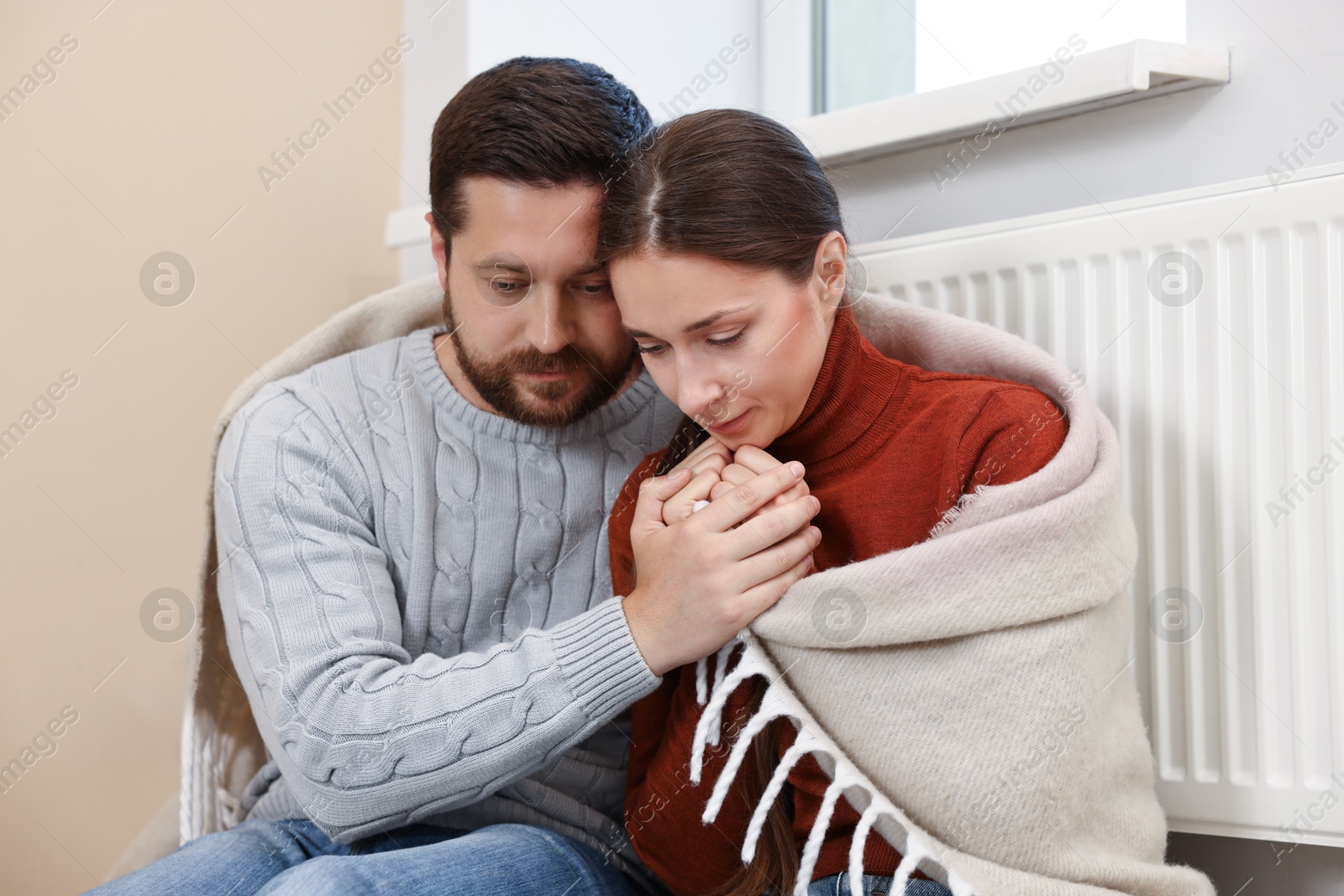 Photo of Couple with blanket warming up near heating radiator at home