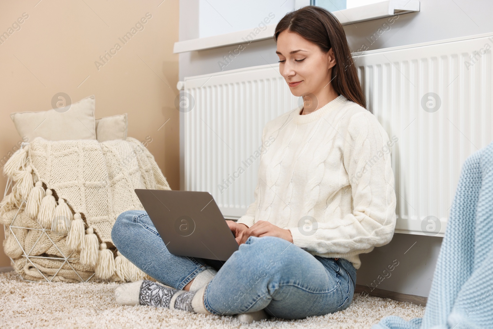 Photo of Happy woman using laptop near heating radiator at home