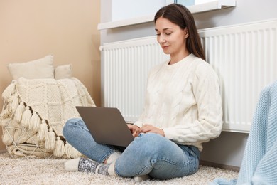 Happy woman using laptop near heating radiator at home