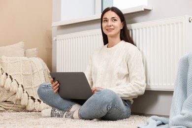 Photo of Happy woman using laptop near heating radiator at home