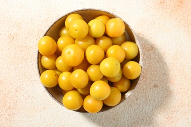 Photo of Tasty ripe plums in bowl on beige textured table, top view