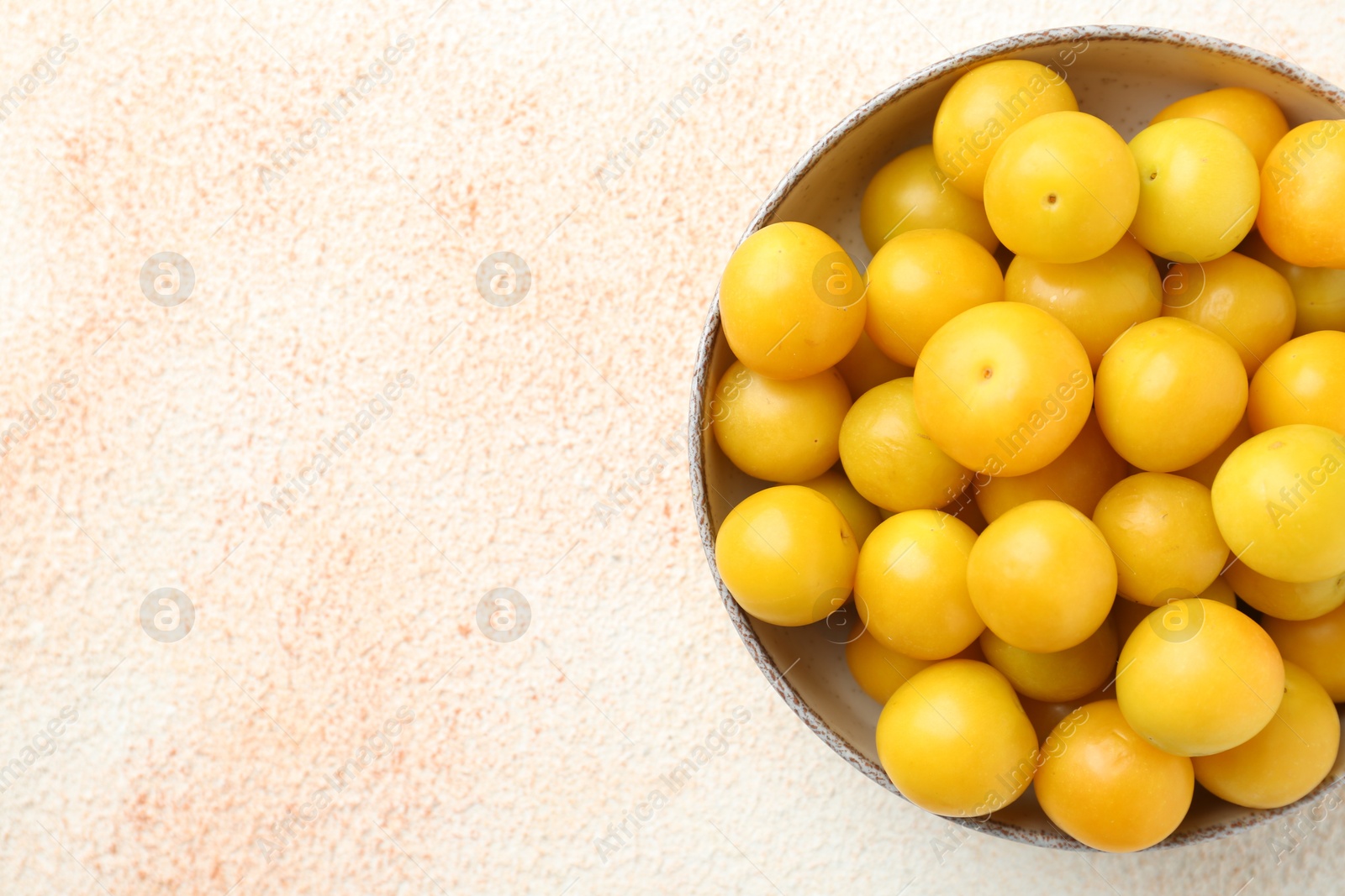 Photo of Tasty ripe plums in bowl on beige textured table, top view. Space for text