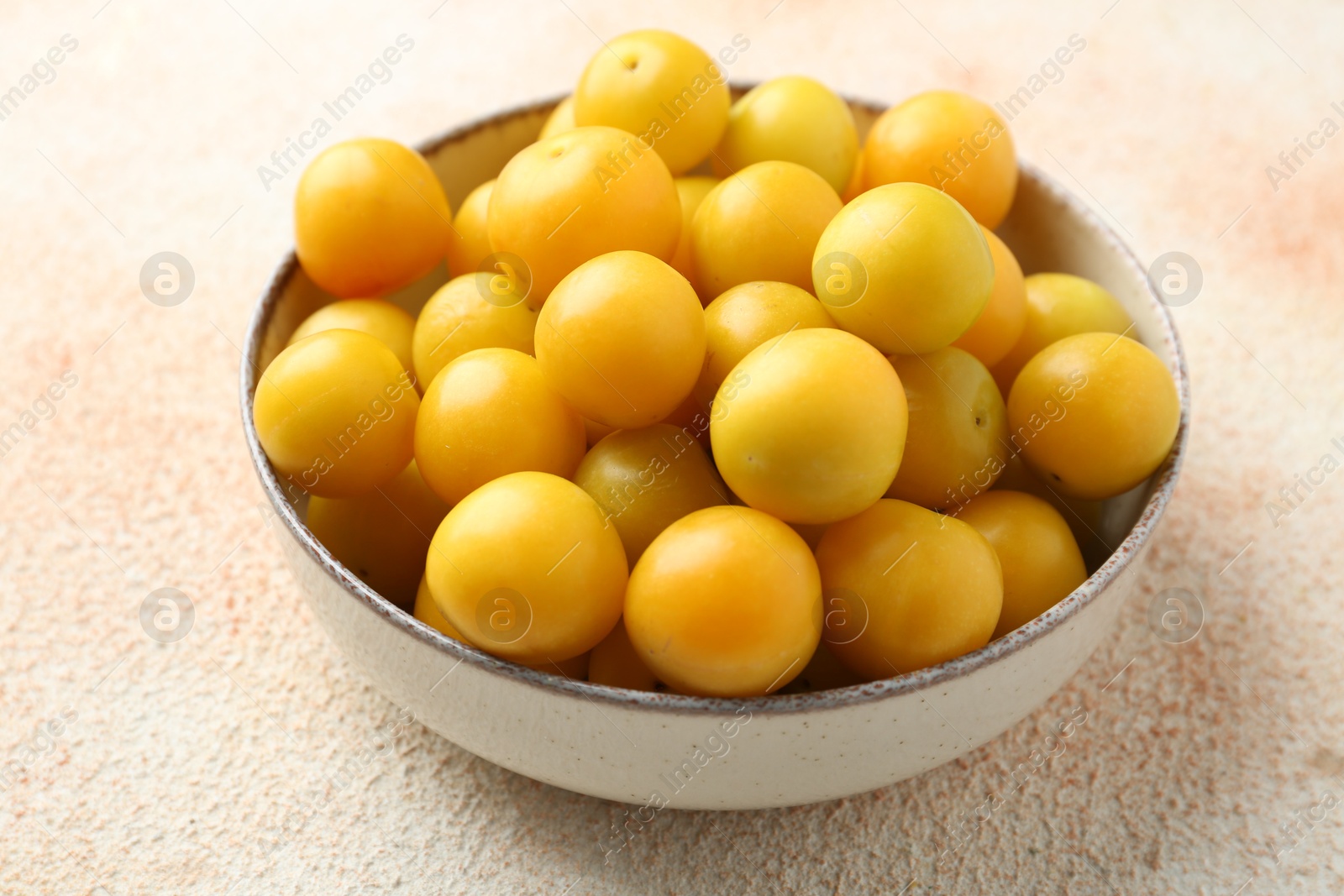 Photo of Tasty ripe plums in bowl on beige textured table, closeup