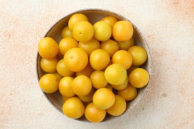 Photo of Tasty ripe plums in bowl on beige textured table, top view