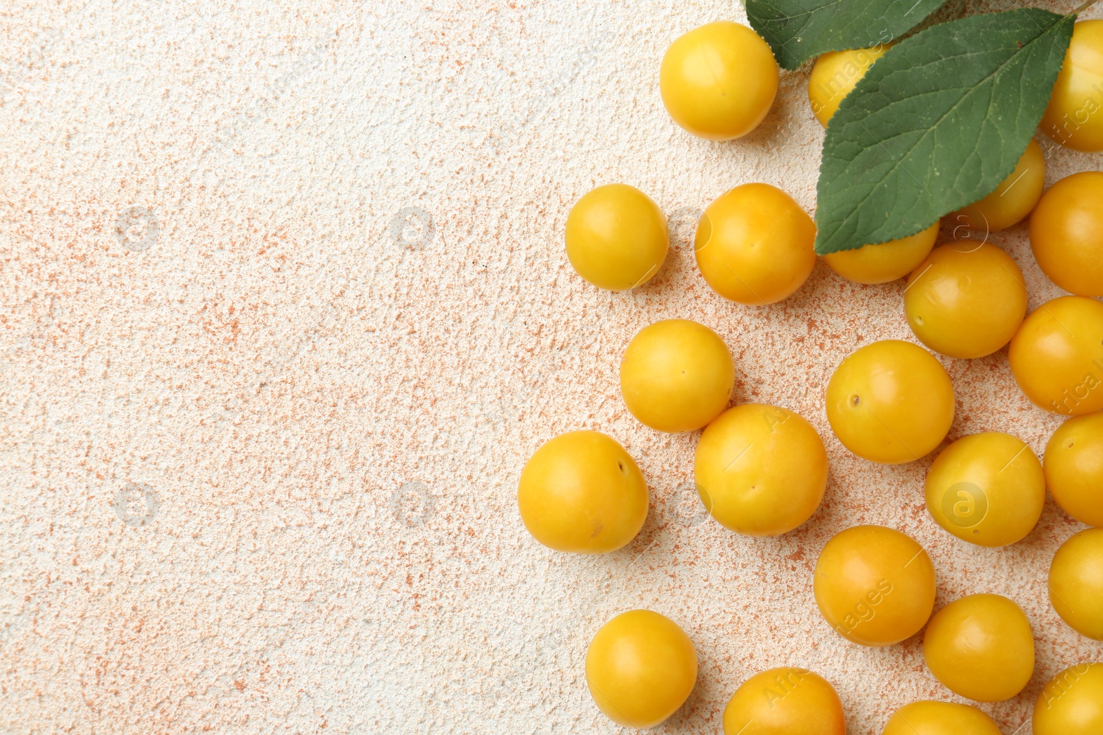 Photo of Tasty ripe plums and leaves on beige textured table, flat lay. Space for text