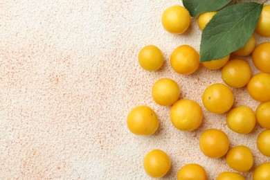 Photo of Tasty ripe plums and leaves on beige textured table, flat lay. Space for text