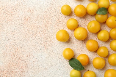 Photo of Tasty ripe plums and leaves on beige textured table, flat lay. Space for text