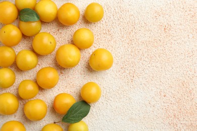 Photo of Tasty ripe plums and leaves on beige textured table, flat lay. Space for text