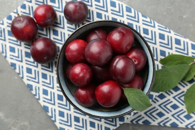 Photo of Tasty ripe plums and leaves in bowl on grey table, flat lay