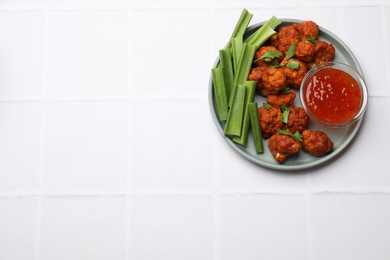 Photo of Baked cauliflower buffalo wings with celery and sauce on white tiled table, top view. Space for text