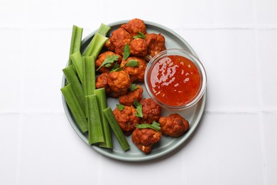 Photo of Baked cauliflower buffalo wings with celery and sauce on white tiled table, top view