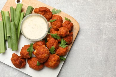 Photo of Baked cauliflower buffalo wings with celery and sauce on grey textured table, top view. Space for text