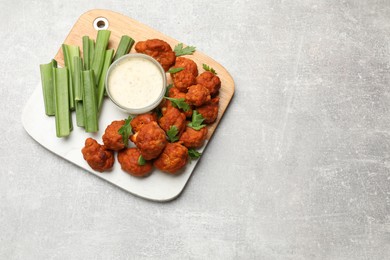 Photo of Baked cauliflower buffalo wings with celery and sauce on grey textured table, top view. Space for text