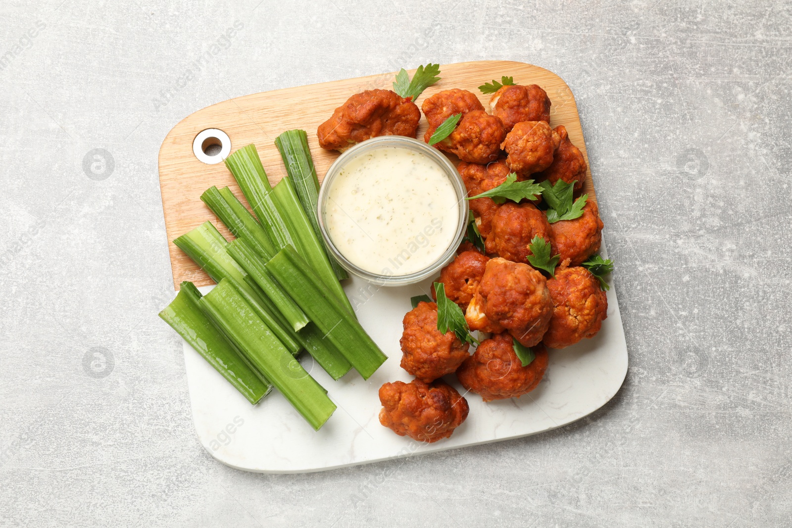 Photo of Baked cauliflower buffalo wings with celery and sauce on grey textured table, top view