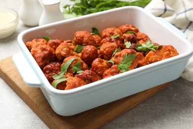 Photo of Baked cauliflower buffalo wings with parsley in baking dish on grey table, closeup