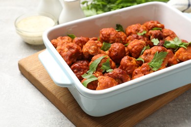 Photo of Baked cauliflower buffalo wings with parsley in baking dish on grey table, closeup