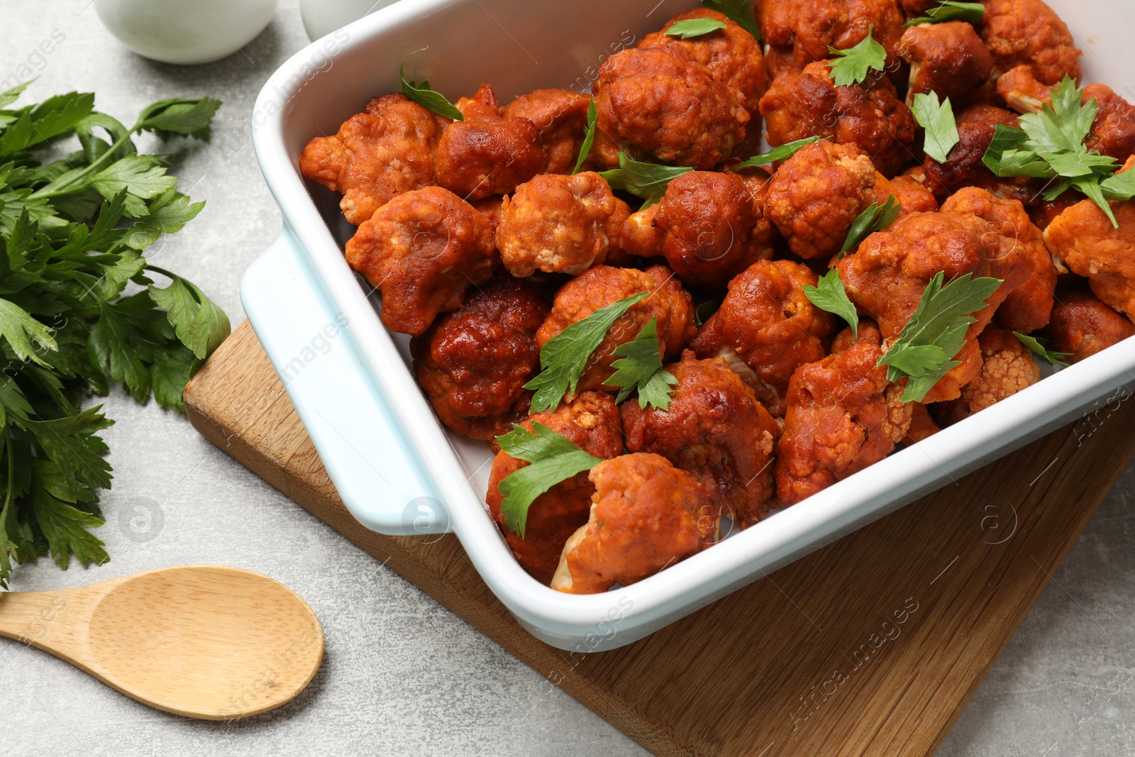 Photo of Baked cauliflower buffalo wings with parsley in baking dish on grey table