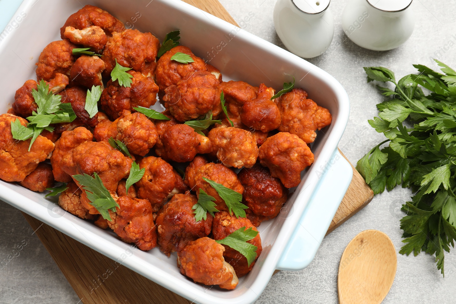 Photo of Baked cauliflower buffalo wings with parsley served on grey textured table, flat lay