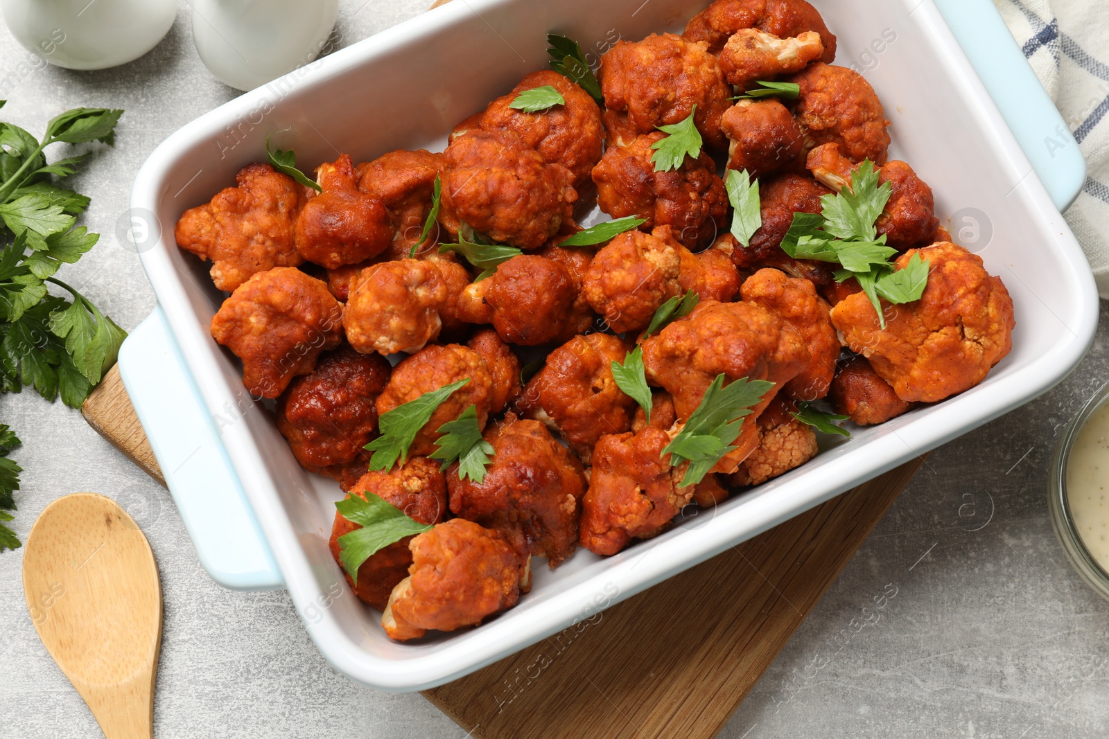 Photo of Baked cauliflower buffalo wings with parsley served on grey textured table, flat lay