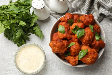 Photo of Baked cauliflower buffalo wings with parsley served on grey textured table, flat lay