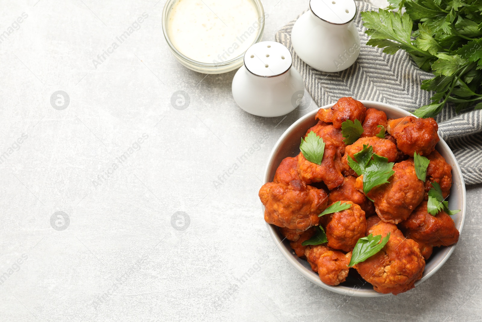 Photo of Baked cauliflower buffalo wings with parsley served on grey textured table, flat lay. Space for text