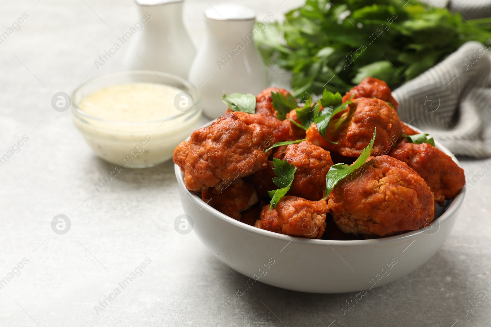 Photo of Baked cauliflower buffalo wings with parsley served on grey textured table, closeup