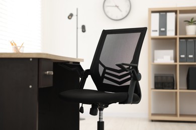 Black chair and wooden desk in office, closeup