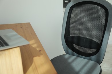 Grey chair, laptop and desk in office, closeup