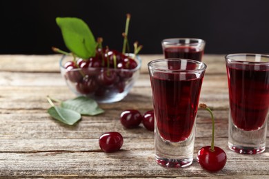 Shot glasses of delicious cherry liqueur and juicy berries on wooden table, closeup