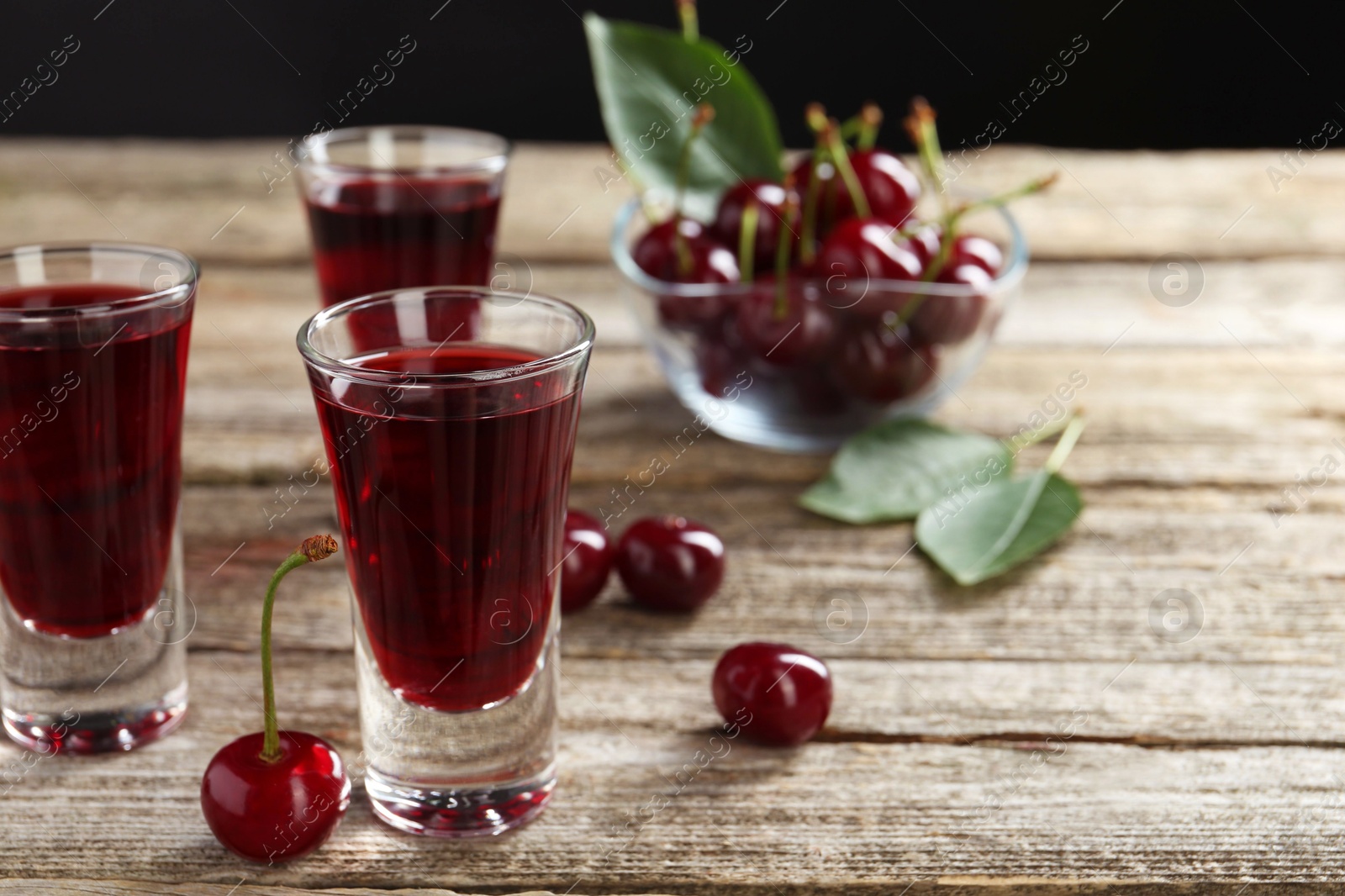 Photo of Shot glasses of delicious cherry liqueur and juicy berries on wooden table, closeup