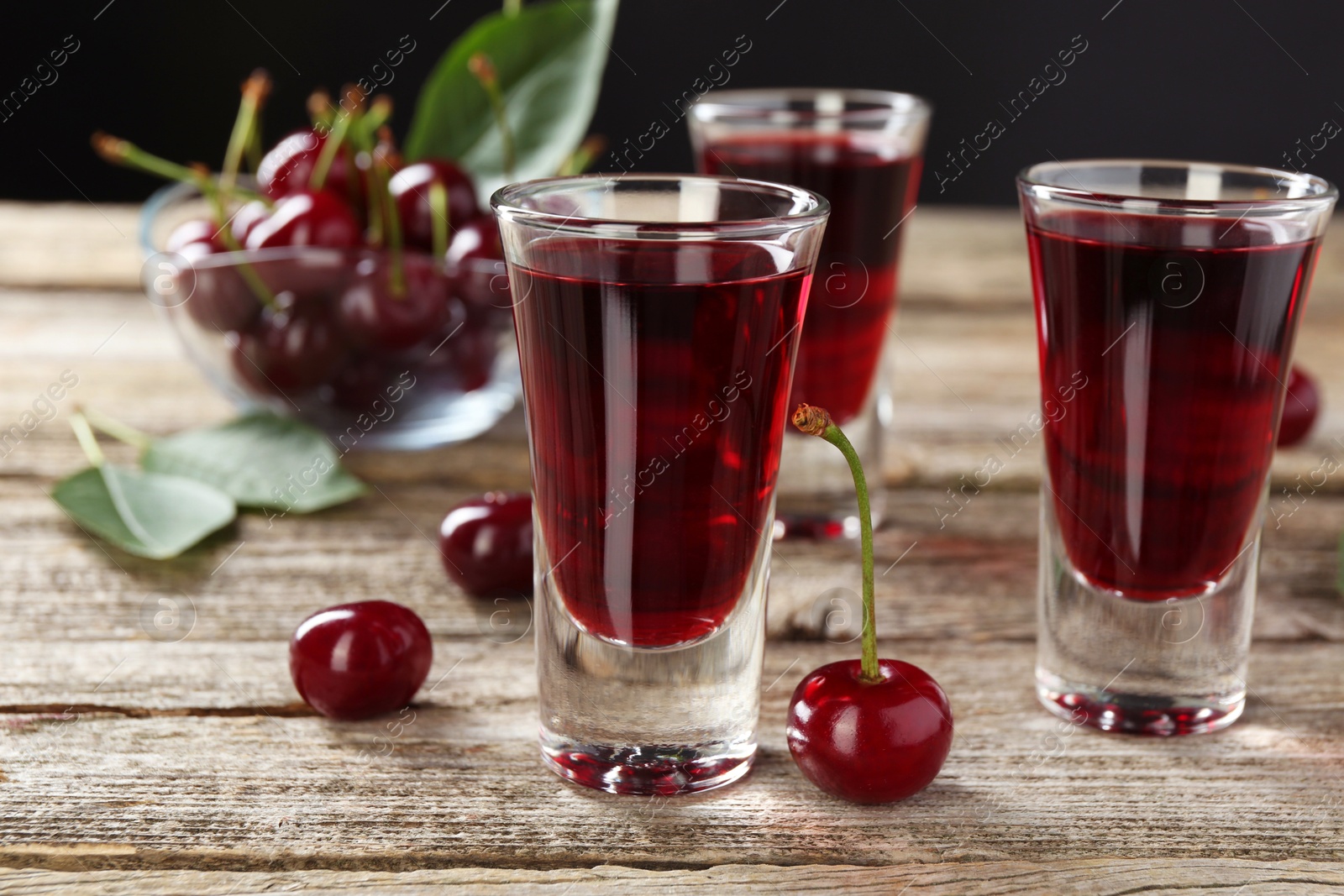 Photo of Shot glasses of delicious cherry liqueur and juicy berries on wooden table, closeup