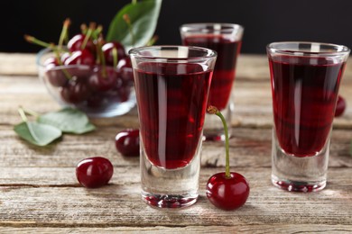 Photo of Shot glasses of delicious cherry liqueur and juicy berries on wooden table, closeup