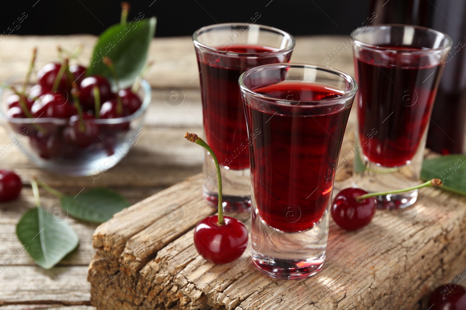 Photo of Shot glasses of delicious cherry liqueur and juicy berries on wooden table, closeup