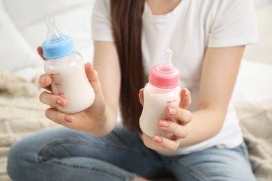 Expecting twins. Pregnant woman holding two bottles with milk at home, closeup