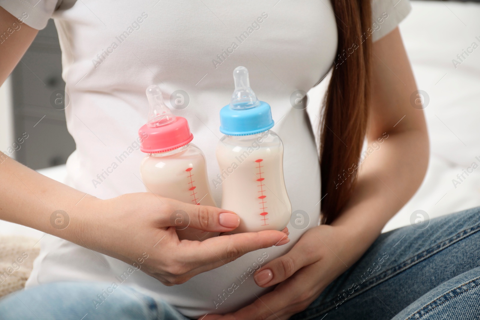 Photo of Expecting twins. Pregnant woman holding two bottles with milk at home, closeup