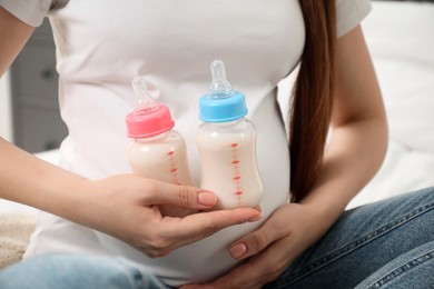 Expecting twins. Pregnant woman holding two bottles with milk at home, closeup