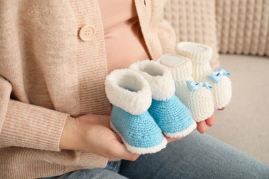 Photo of Expecting twins. Pregnant woman holding two pairs of shoes at home, closeup