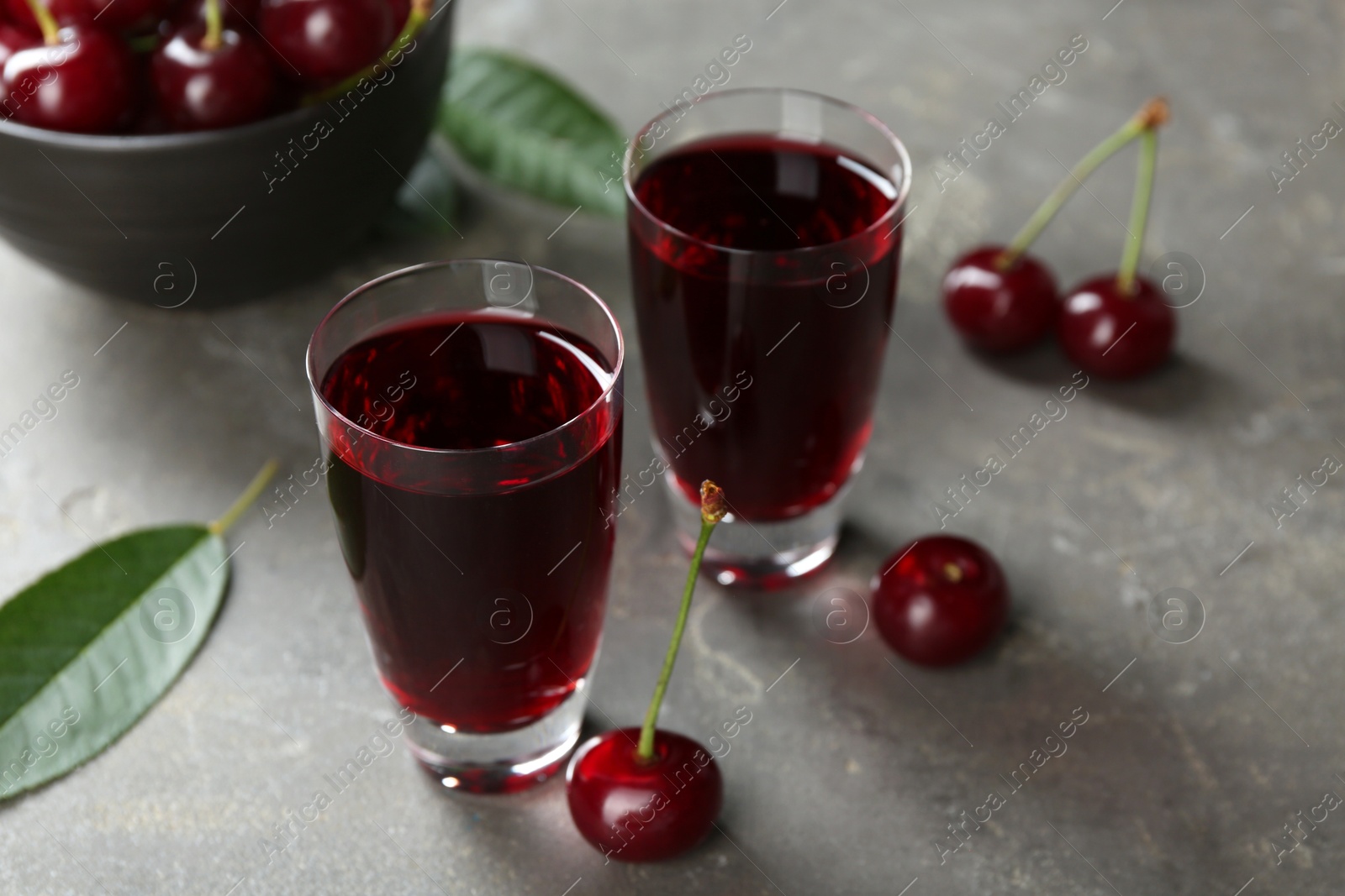 Photo of Delicious cherry liqueur in shot glasses and fresh berries on grey table